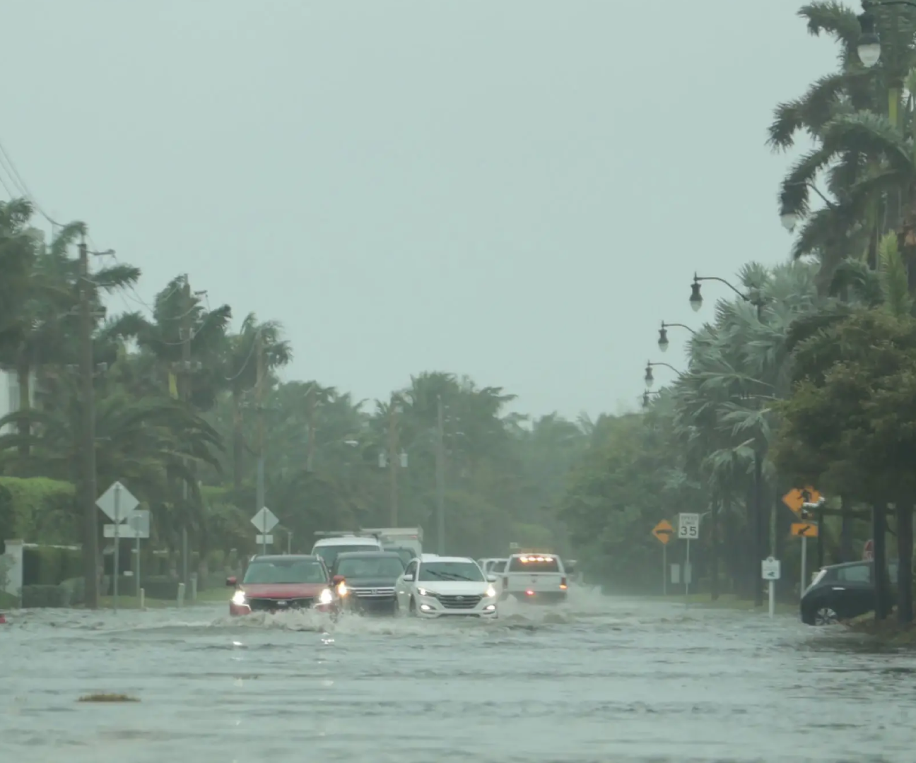 Cars driving through a heavily flooded street in rainy weather.